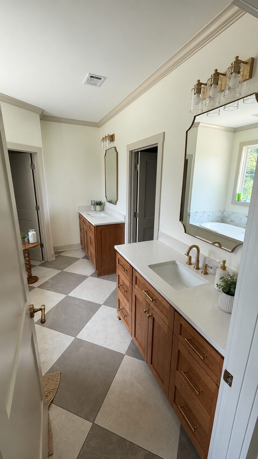 Master bathroom remodel with twin oak vanities, quartz countertops, a grey and cream checkerboard tile floor, arched brass mirrors and brass fixtures.