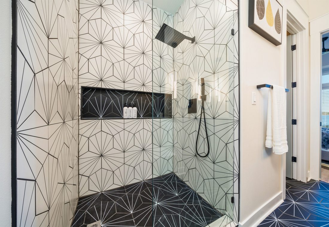 Walk-in shower tiled in white starburst geometric tile with a contrasting black tiled niche, matte black fixtures and a frameless glass door.