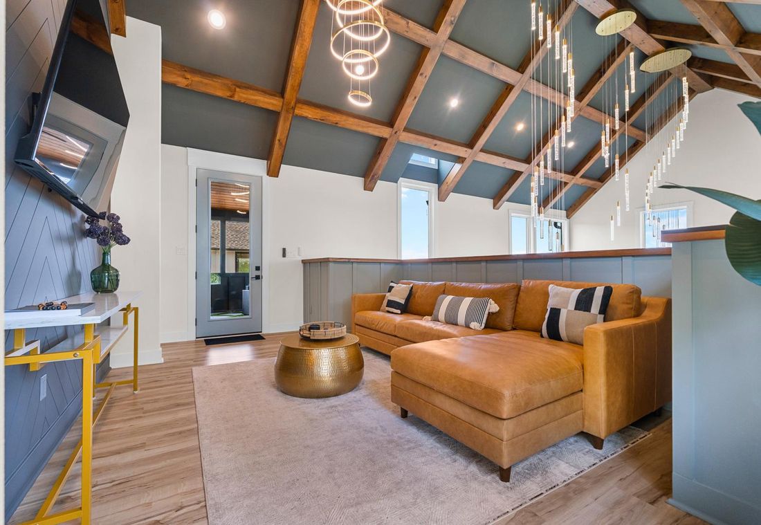 Living room remodel with a vaulted ceiling, exposed stained wood beams, board-and-batten wainscoting and wide plank flooring.