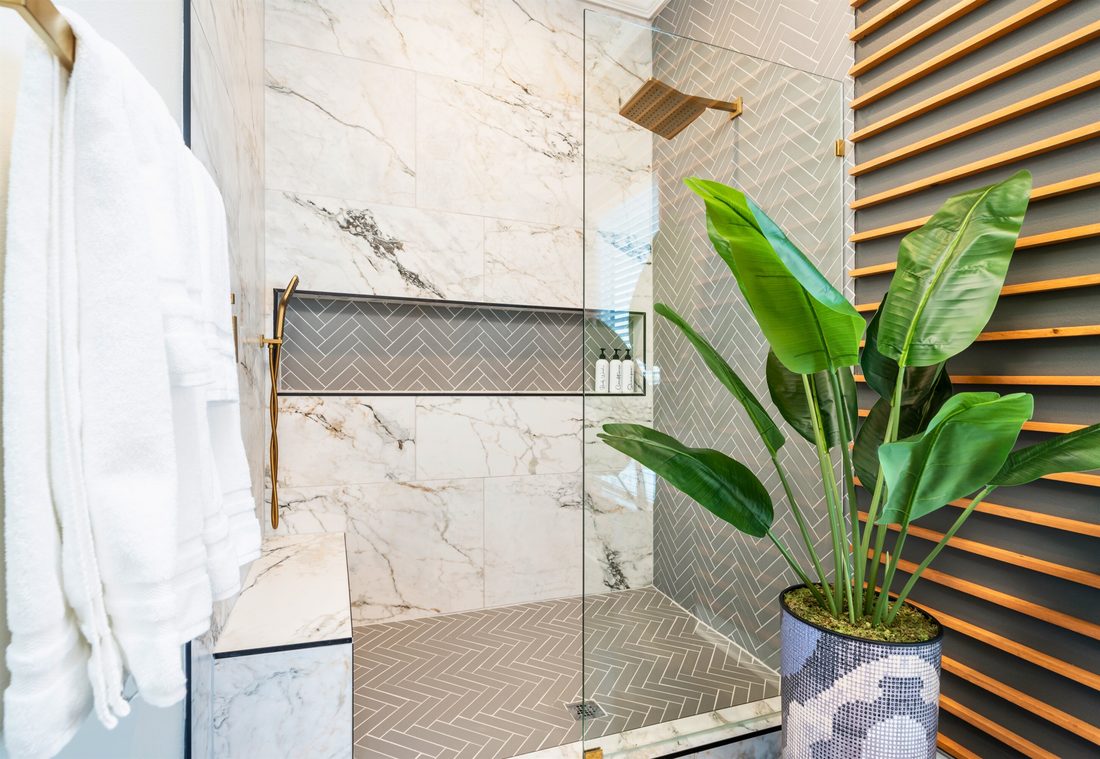 Walk-in shower with large-format marble-look tile, a grey herringbone accent wall and floor, a full-width niche, marble bench and brass fixtures.