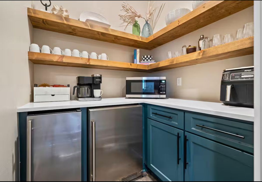Butler pantry and coffee bar with teal cabinetry, floating wood corner shelves, quartz counters and two stainless beverage refrigerators.