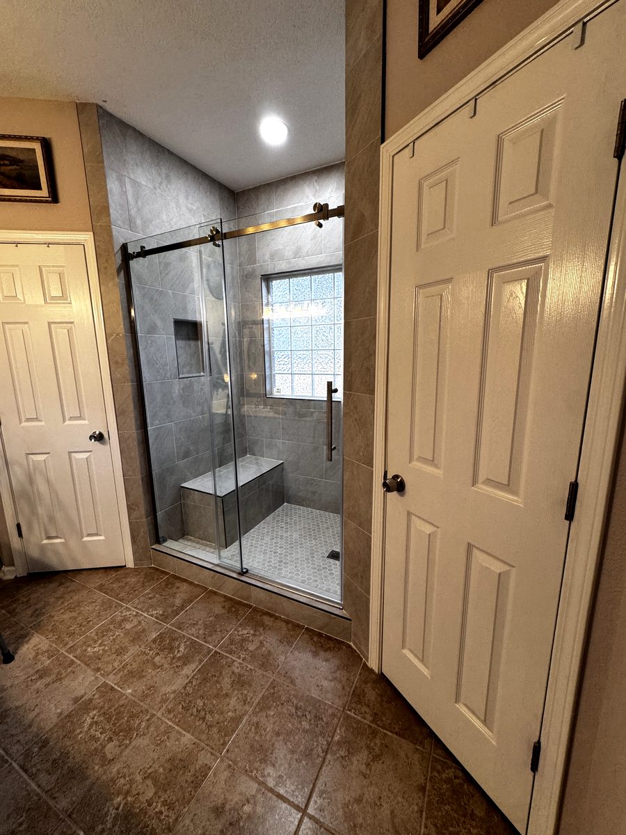 Walk-in tile shower with a sliding frameless glass door, built-in bench seat, recessed niche and a white hexagon mosaic floor.